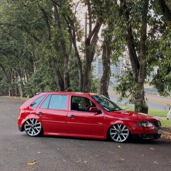 Gol G4 vermelho rebaixado visto de lado, entre árvores
